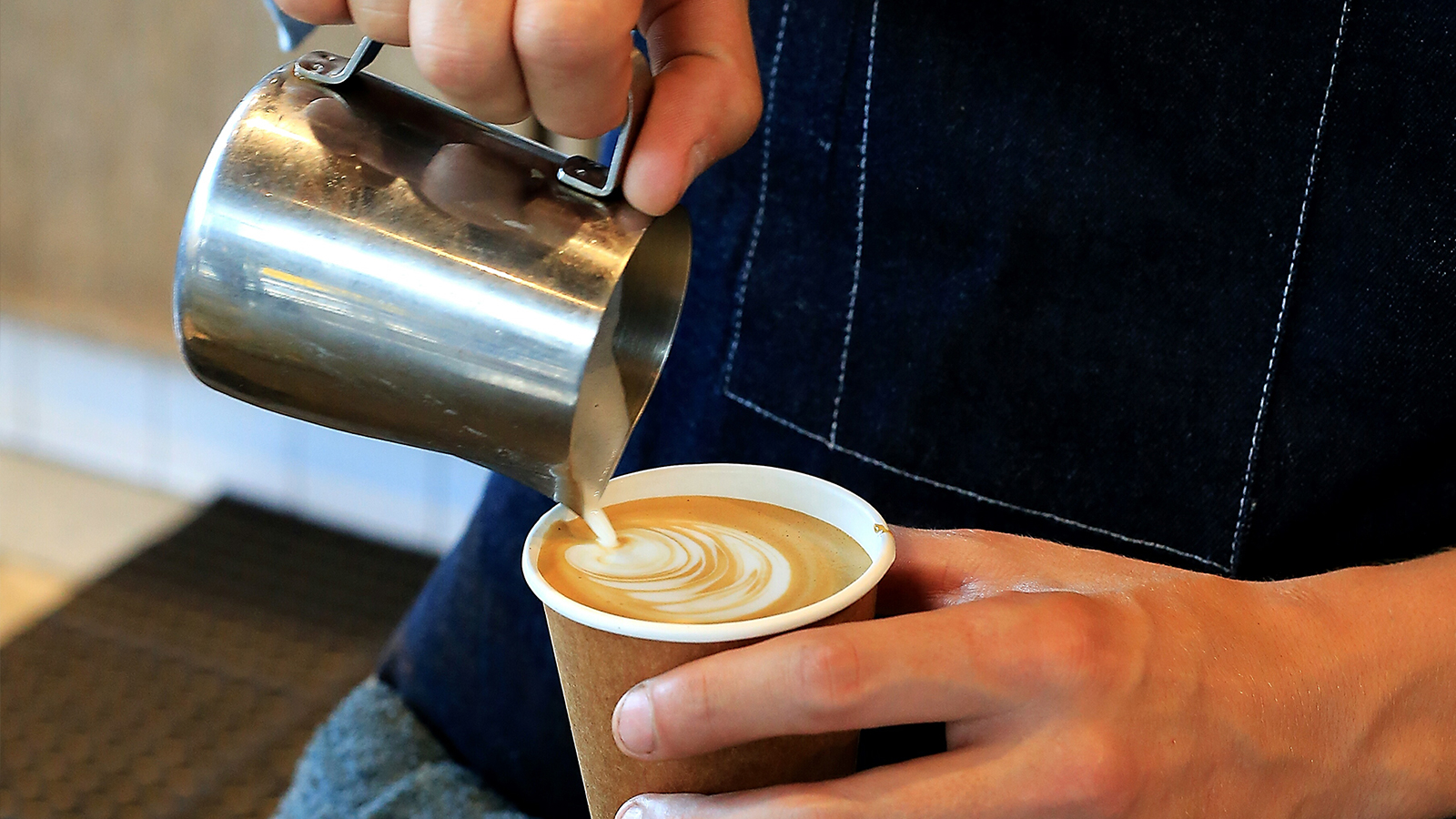 Barista adding steamed milk to expresso making a Cappuccino.