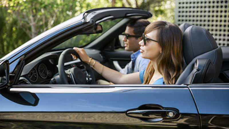 A woman driving a black convertible car and a man in the passenger seat.